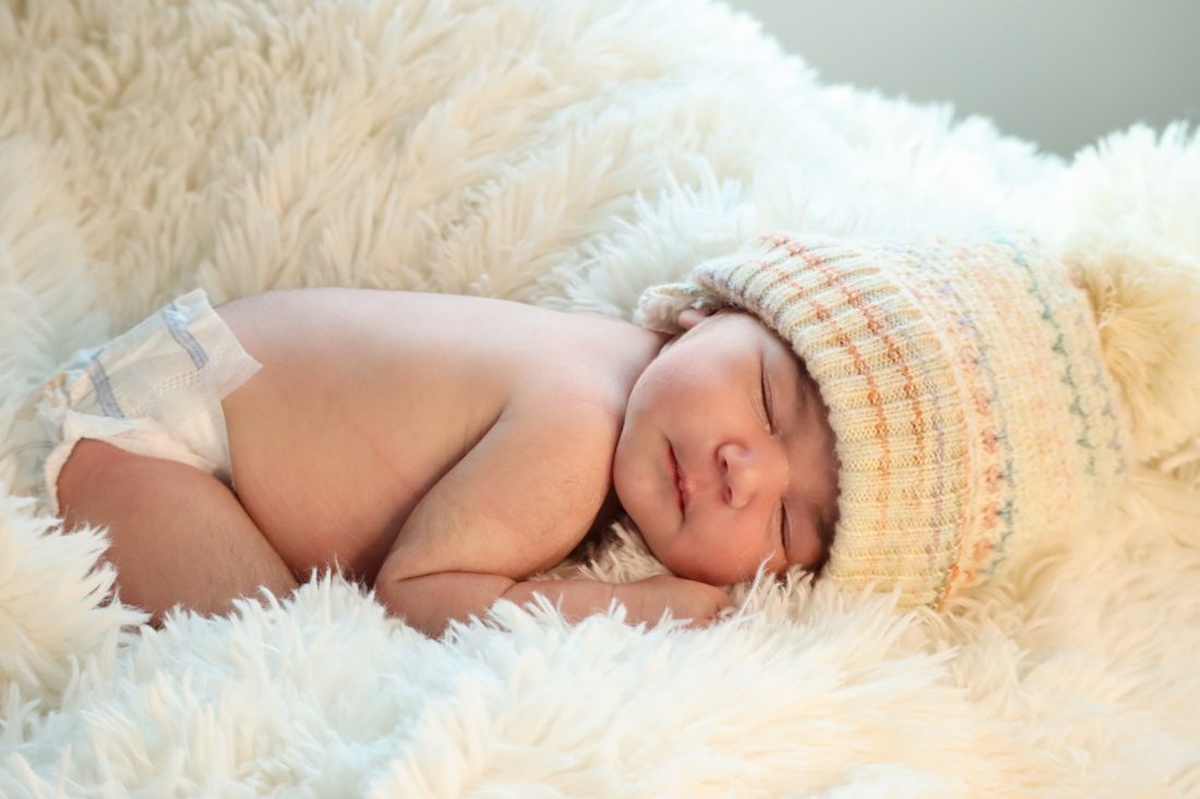 Bebé dormido con un gorro tejido sobre una manta blanca